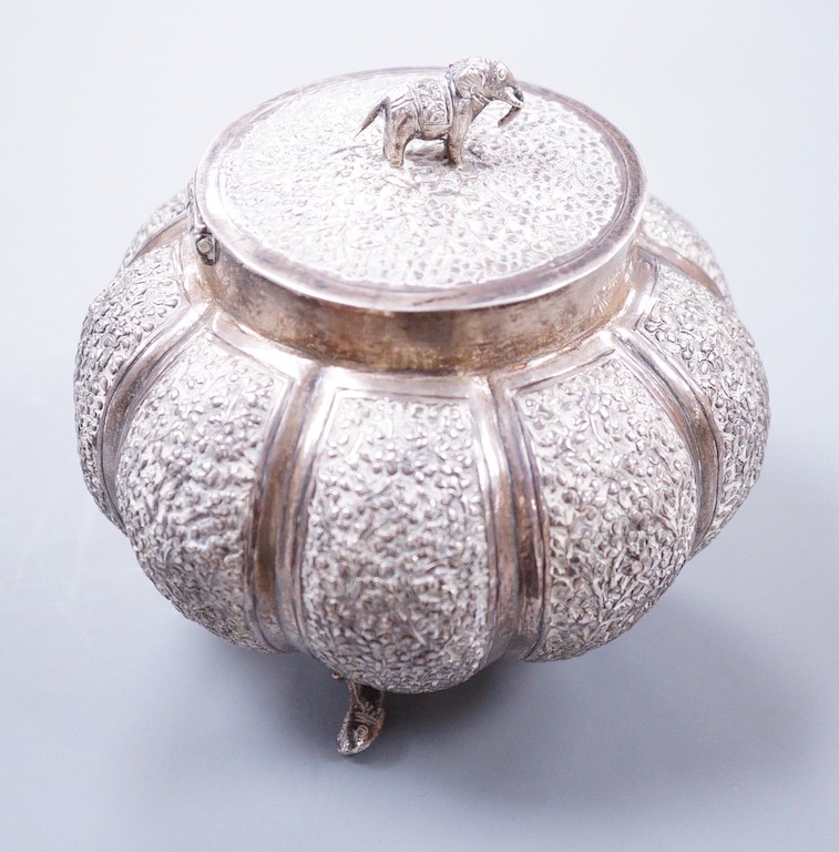 An Indian embossed lobed white metal circular pot and cover, with elephant finial, on three dolphin feet, height 10cm, 197 grams.
